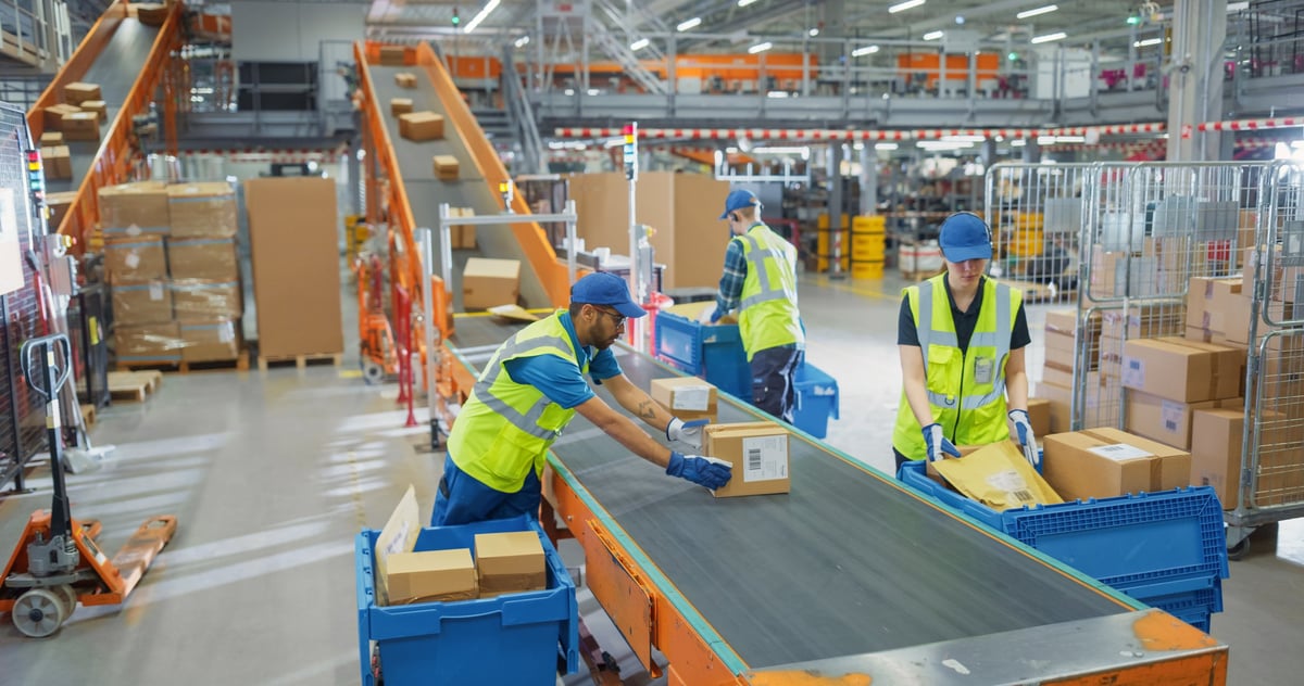 Warehouse team organizing parcels on a conveyor in safety vests